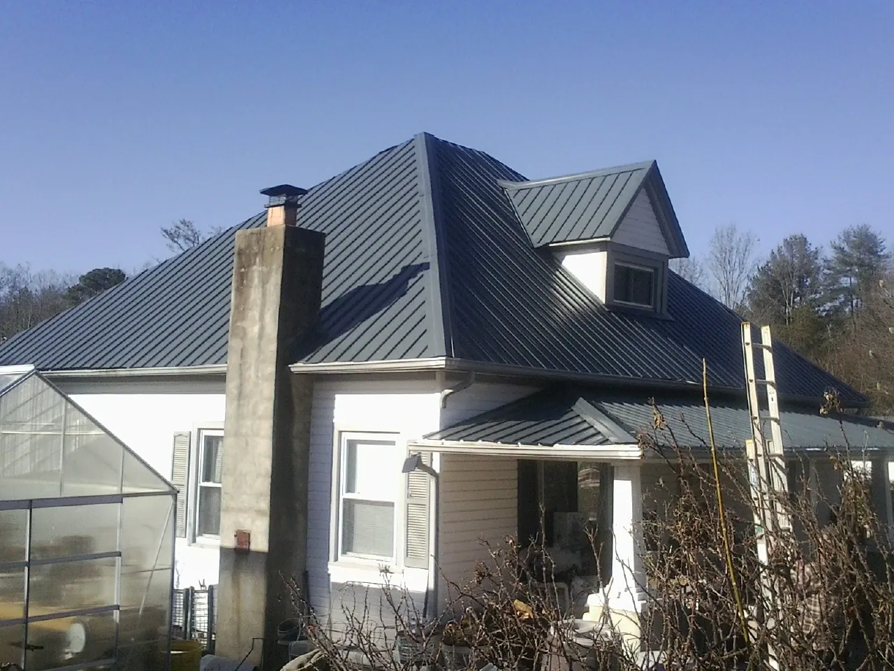 Dark blue standing seam metal roof on a white farmhouse with dormer — Slate & Tile Roof Repair by Roofing Brothers in Winterset