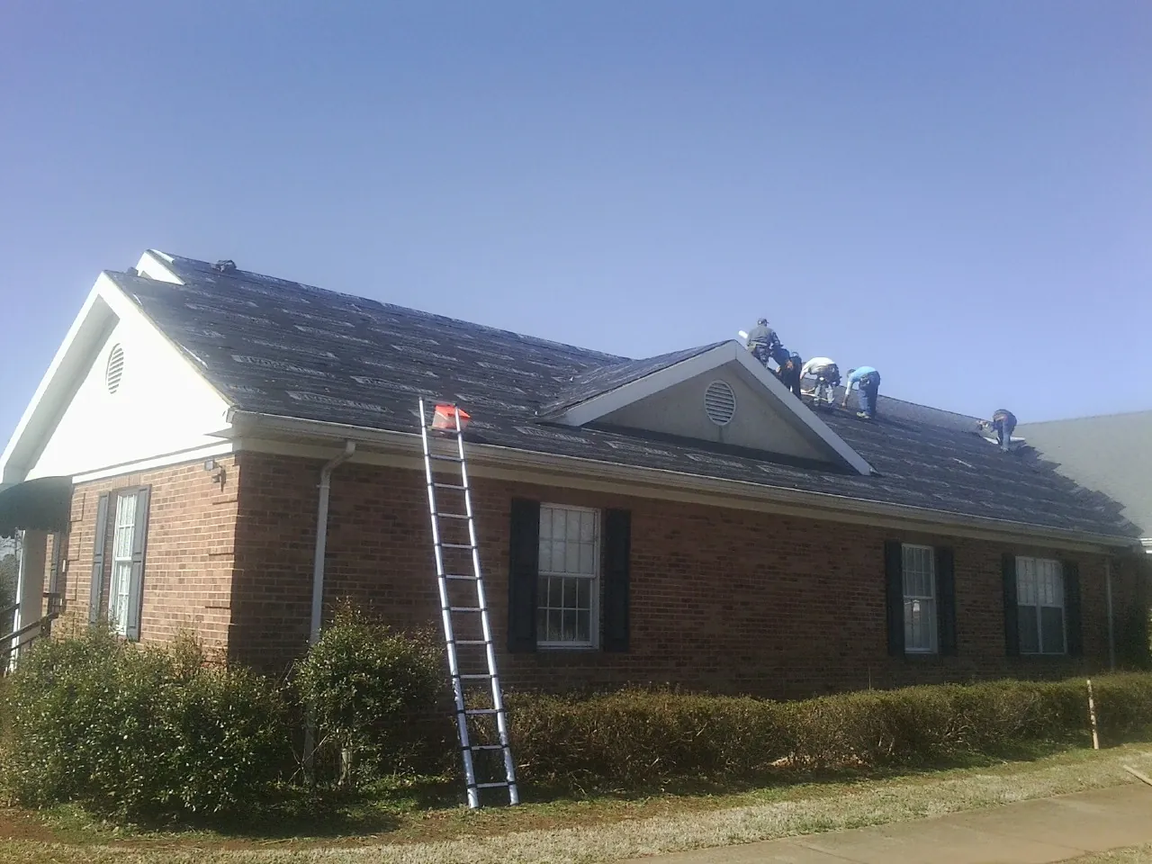 Crew tearing shingles off a brick ranch roof with a ladder set — Emergency Roof Repair work by our crew in Winterset