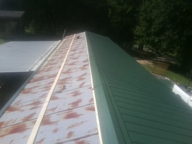 Old rusted panels beside newly installed green metal roofing — Wind Damage Roof Repair by Roofing Brothers in Winterset