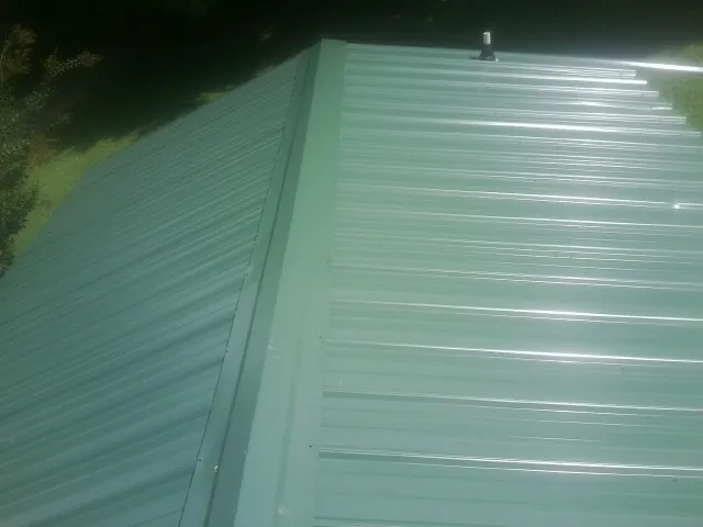 New green metal panels meeting at the ridge of a roof — Flat Roof Repair work by our crew in Winterset