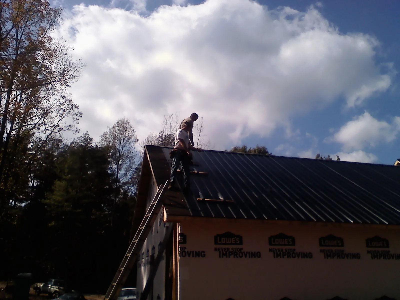Roofer fastening dark metal panels high against a cloudy sky, from a Roof Inspection job in Winterset