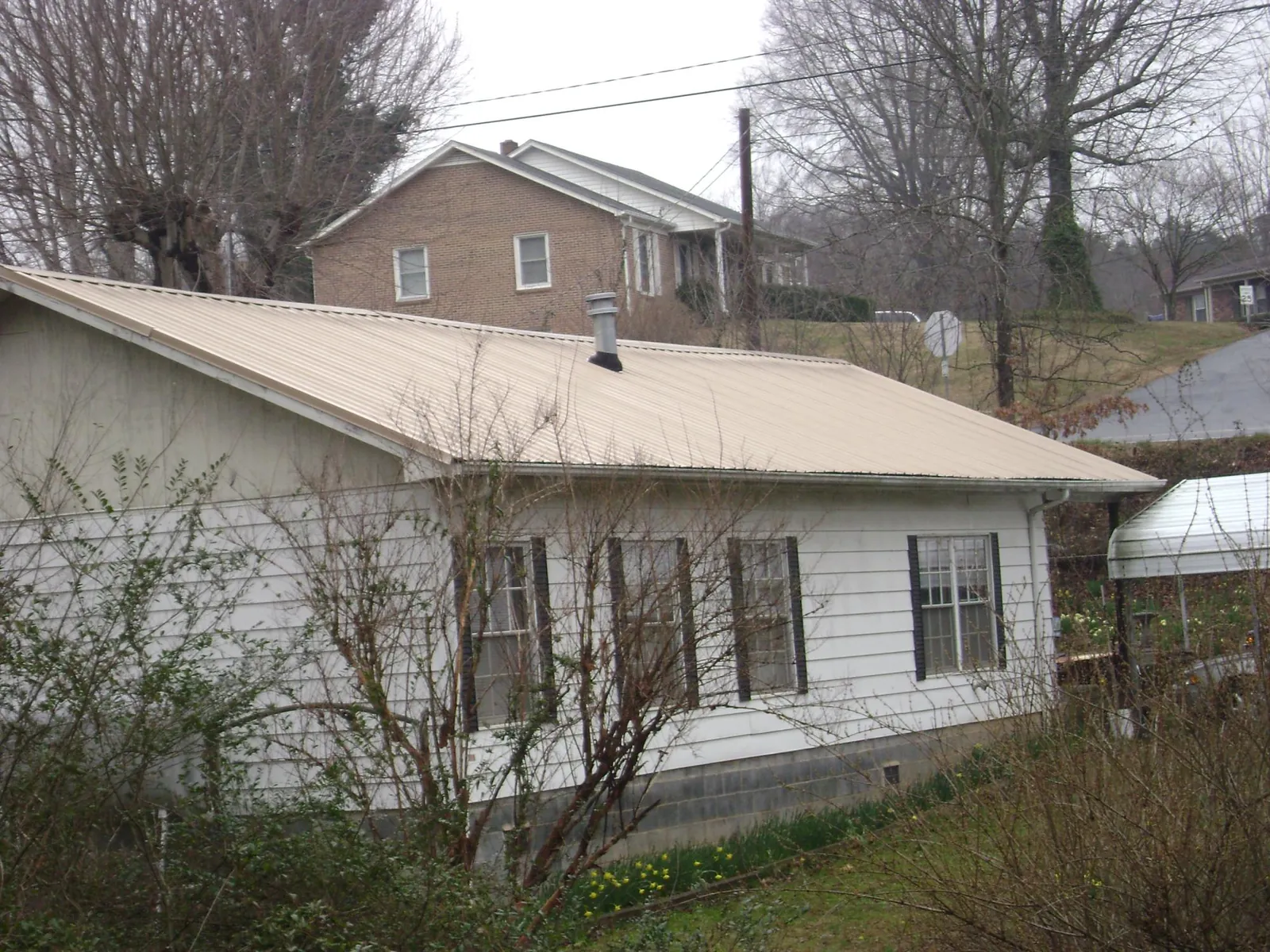 Tan metal roof on a white sided house set into a hillside — Commercial Roofing by Roofing Brothers in Winterset