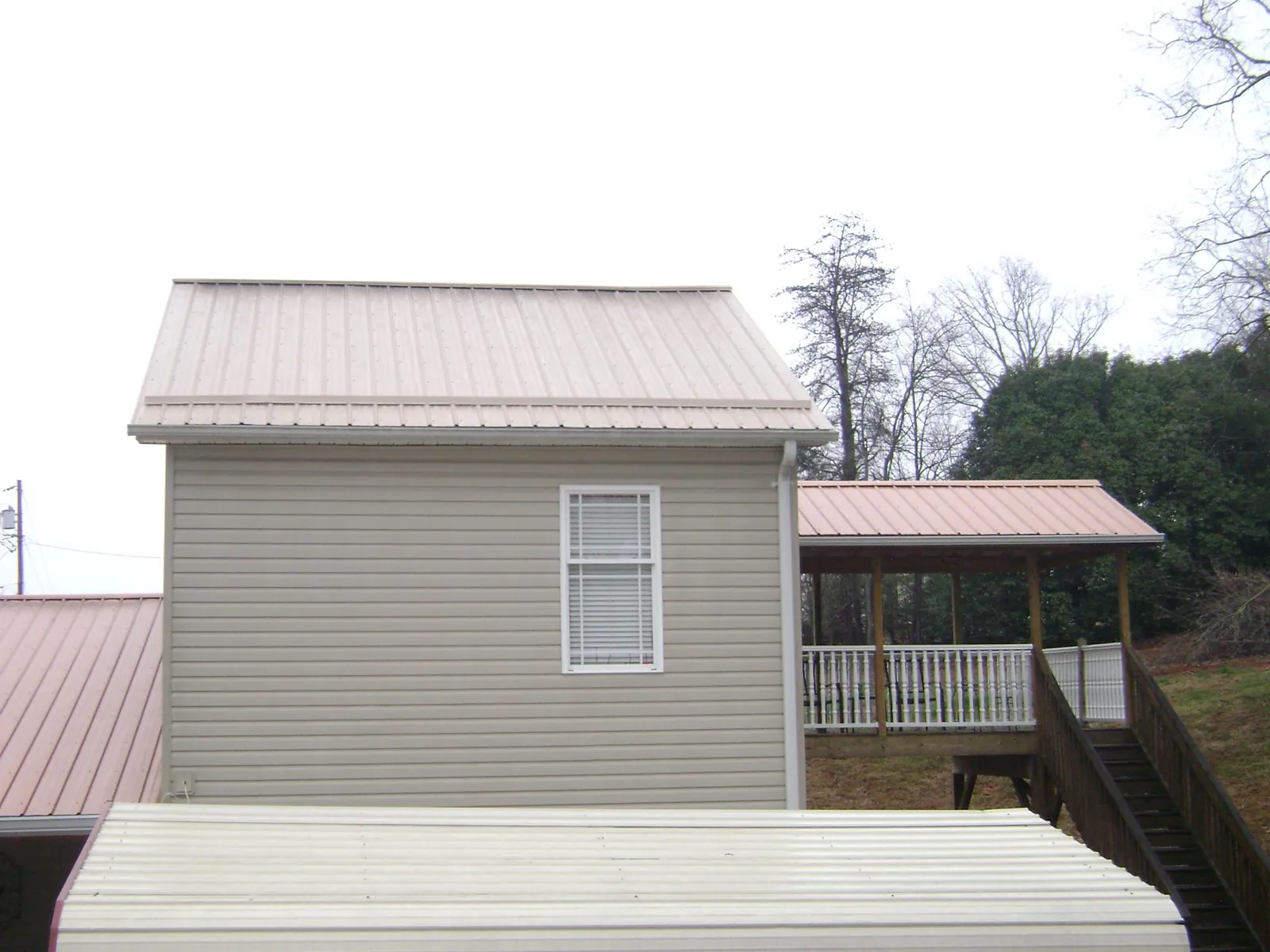 Tan metal roofs on a two story addition and attached porch, from a Roof Replacement job in Winterset